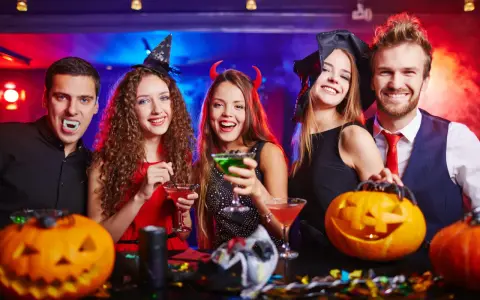 Glada vuxna firar halloween med drinkar och pumpor. En vampyr, en häxa och en djävul njuter av festen. Perfekt för halloween lekar vuxna!