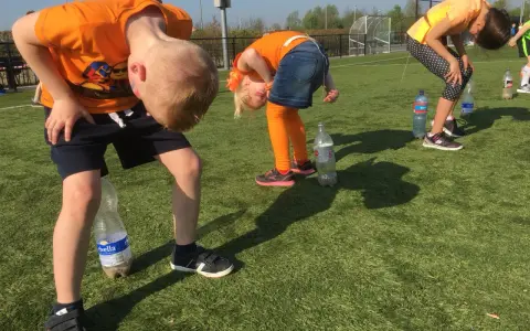 Barn i orange kläder böjer sig framåt för att försöka fånga en flaska med munnen. En del av kalas lekarna.