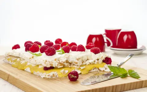 En läcker rice krispies tårta med hallon och citronkräm, redo att serveras med röda muggar i bakgrunden.