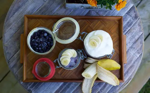 En bricka med ingredienser för sommarmat recept: blåbär, yoghurt, banan och en burk med bär och banan.