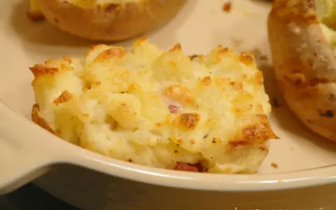 En närbild på en krämig, osttäckt bakad potatis fylld med baconbitar.