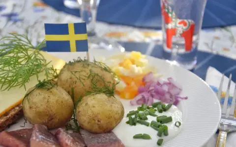 En tallrik med sill, färskpotatis, ost och dill. En svensk flagga vajar stolt. Perfekt mat midsommar!
