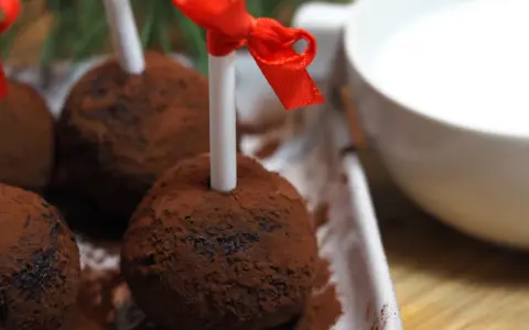 Chokladbollar på pinne, pudrade med kakao, redo att doppas i varm choklad. Röda band pryder pinnarna.