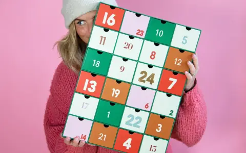 En person med en stickad tröja och mössa håller upp en färgglad julkalender. En perfekt julkalender diy att skapa själv!