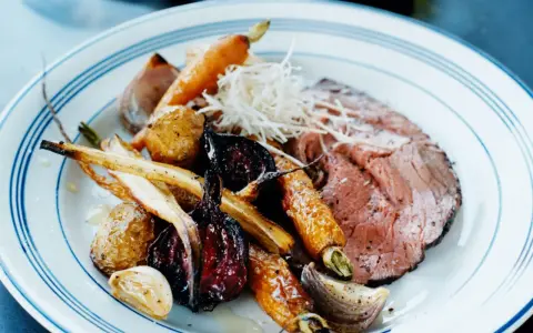 En tallrik med skivad rostbiff, rostade rotfrukter som morötter och palsternacka, samt vitlök. Ett perfekt rostbiff recept för en festmåltid.