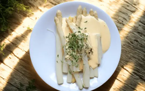 En tallrik med vit sparris, täckt av en krämig sås och toppad med färska groddar. En klassisk svensk vårrätt.