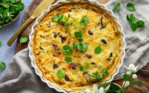 En gyllene kantarellpaj, perfekt för ett höstligt kantarellpaj recept. Garnerad med färska gröna blad och serverad med en gyllene kniv.