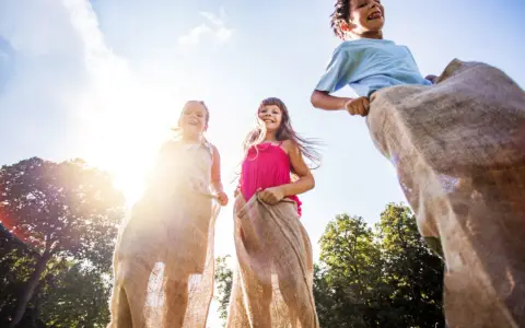 Barn hoppar säcklöpning i solsken, en klassisk midsommaraktivitet. En del av en femkamp midsommar.