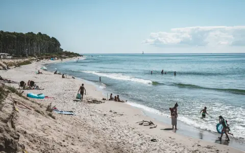 Människor njuter av solen och havet på sveriges finaste strand. En segelbåt syns i fjärran.