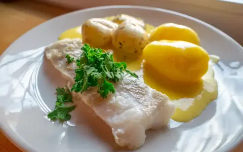 En portion rimmad torsk med kokt potatis och en krämig sås, garnerad med färsk persilja.