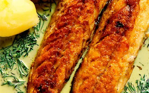 Två gyllene filéer av stekt makrill i en krämig sås med dill och kokt potatis.