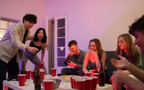Unga vänner spelar beer pong, en rolig aktivitet med röda muggar och skratt.
