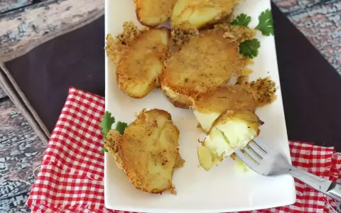Krispiga, gyllene smashed potatis på en vit tallrik, garnerade med persilja. En gaffel visar en mjuk insida.