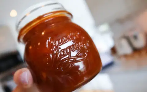 En hand håller ett glas med en mörkröd rabarber chutney.
