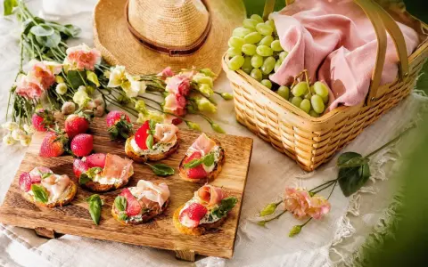 En härlig picknick med bruschetta toppad med jordgubbar och parmaskinka, färska jordgubbar, vindruvor i korg och en stråhatt.