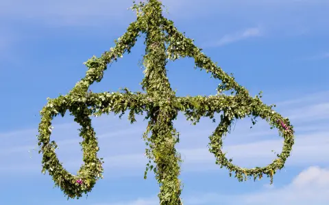 En midsommarstång, dekorerad med grönska och blommor, mot en blå himmel. En symbol för sommar och glädje, en viktig del av fakta om midsommar.