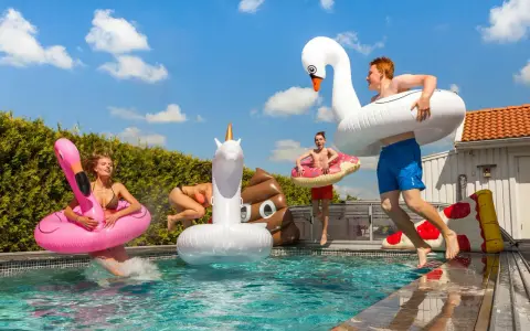 Ungdomar hoppar i poolen med uppblåsbara badleksaker som flamingo, enhörning och bajskorv. Perfekt för midsommarlekar inomhus eller utomhus!