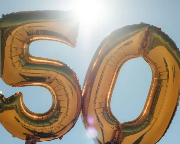 Gyllene ballonger formar siffran 50 mot en klarblå himmel. Perfekt för roliga frågor till 50 års fest!
