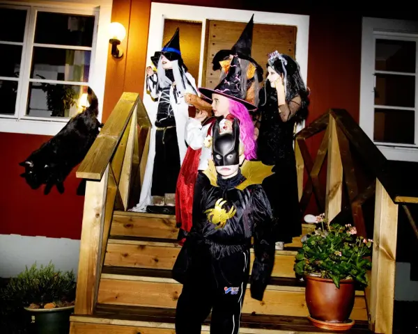 Barn utklädda till häxor och Batman förbereder sig för halloween helg. En svart katt smyger på trappan.