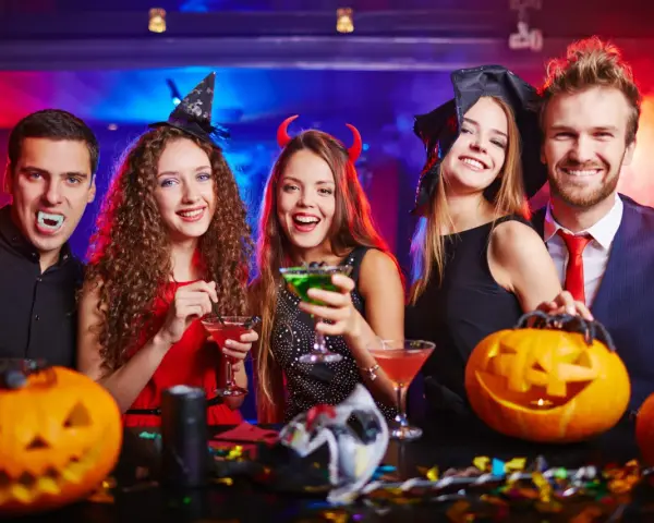Glada vuxna firar halloween med drinkar och pumpor. En vampyr, en häxa och en djävul njuter av festen. Perfekt för halloween lekar vuxna!