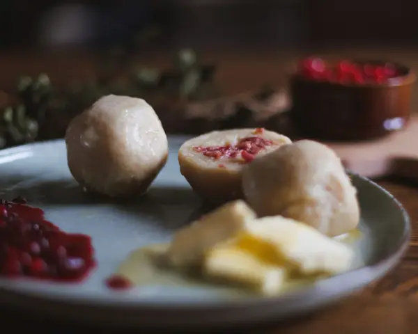 En tallrik med pitepalt, lingonsylt och smör. En halv palt visar en fyllning av fläsk. Perfekt för ett recept på pitepalt.
