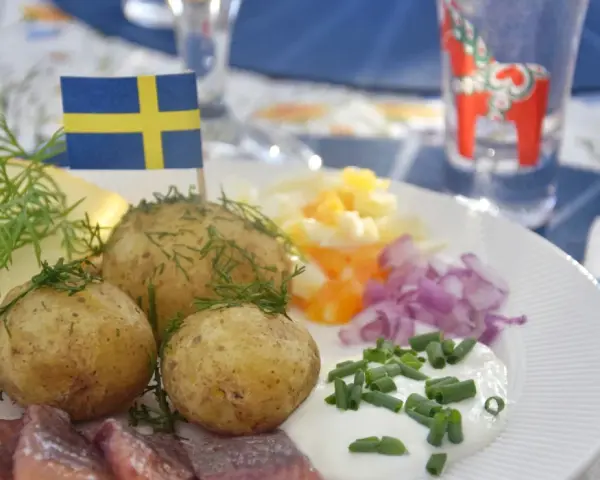 En tallrik med sill, färskpotatis, ost och dill. En svensk flagga vajar stolt. Perfekt mat midsommar!