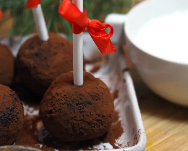 Chokladbollar på pinne, pudrade med kakao, redo att doppas i varm choklad. Röda band pryder pinnarna.