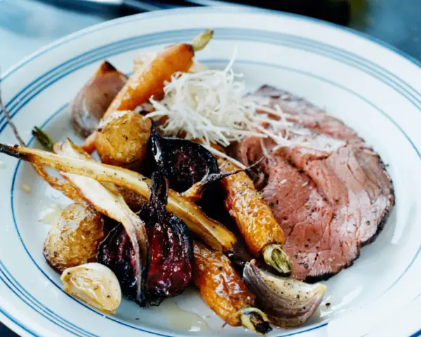 En tallrik med skivad rostbiff, rostade rotfrukter som morötter och palsternacka, samt vitlök. Ett perfekt rostbiff recept för en festmåltid.