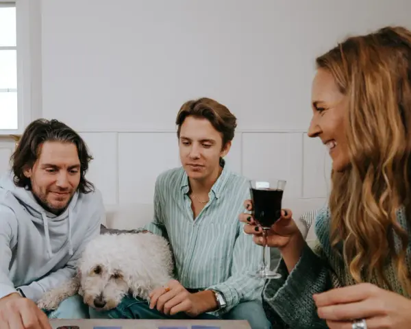 Familj spelar julklappsspelet. Alla får en julklapp, men reglerna kan vara knepiga! En vit hund vilar på soffan.