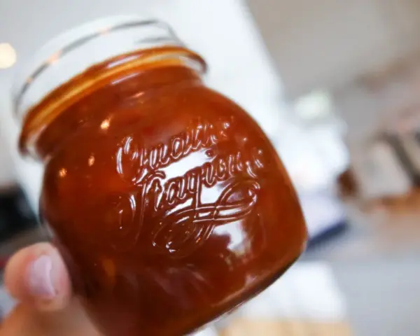 En hand håller ett glas med en mörkröd rabarber chutney.