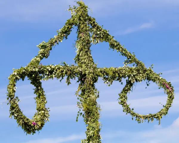En midsommarstång, dekorerad med grönska och blommor, mot en blå himmel. En symbol för sommar och glädje, en viktig del av fakta om midsommar.