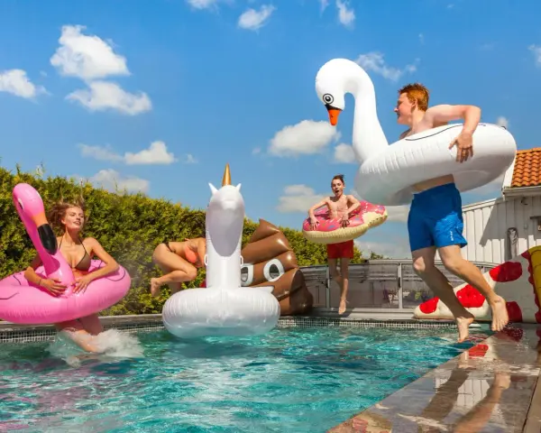 Ungdomar hoppar i poolen med uppblåsbara badleksaker som flamingo, enhörning och bajskorv. Perfekt för midsommarlekar inomhus eller utomhus!