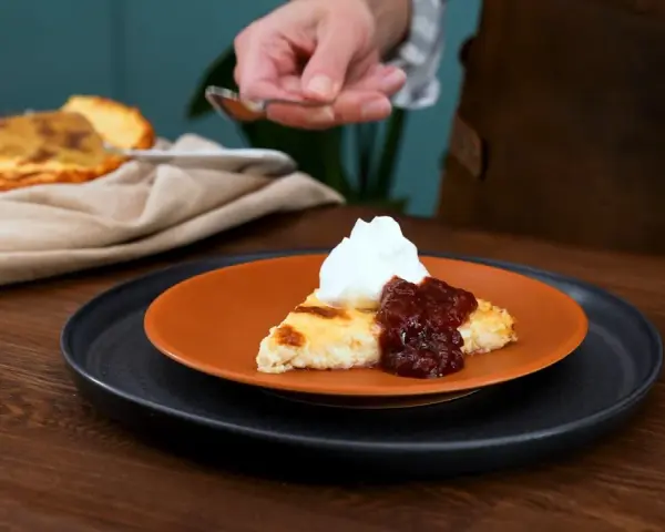 En bit ostkaka med vispad grädde och sylt. Ett perfekt ostkaka recept för fikat.