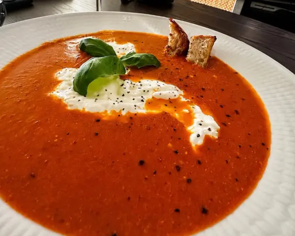 En krämig tomatsoppa med en klick gräddfil, färsk basilika och krutonger. Perfekt som en del av ett tomatsoppa recept.