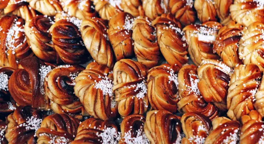 En stor hög med gyllene kanelbullar, perfekta för kanelbullens dag. Strösslade med pärlsocker.