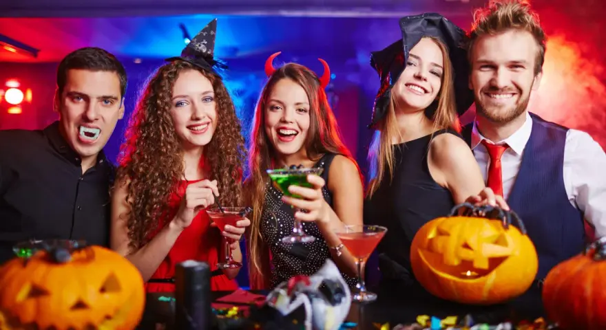Glada vuxna firar halloween med drinkar och pumpor. En vampyr, en häxa och en djävul njuter av festen. Perfekt för halloween lekar vuxna!