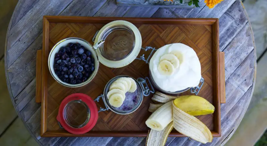 En bricka med ingredienser för sommarmat recept: blåbär, yoghurt, banan och en burk med bär och banan.