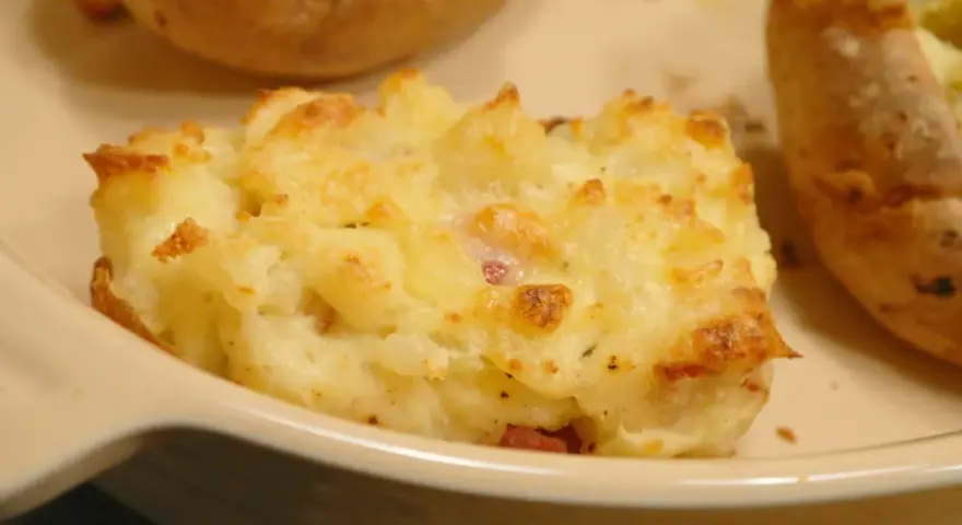 En närbild på en krämig, osttäckt bakad potatis fylld med baconbitar.