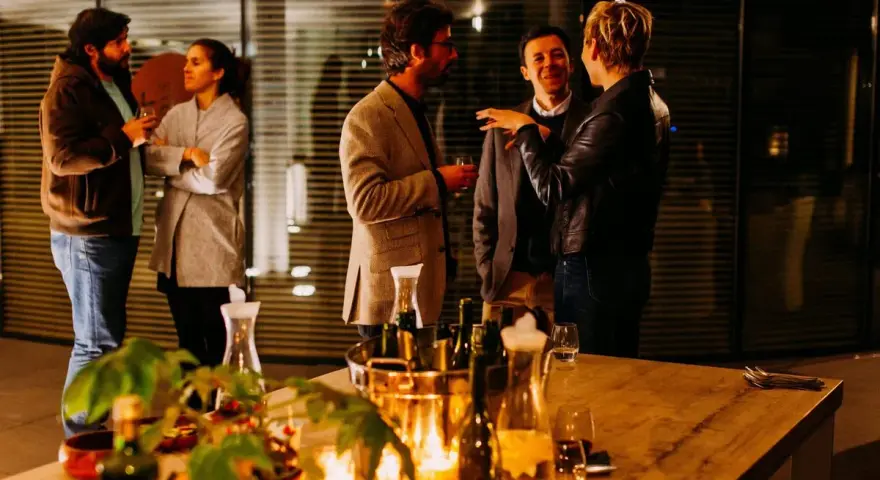 Folk minglar och skrattar under en mysig julfest på jobbet. Ett bord med dryck och ljus skapar stämning.