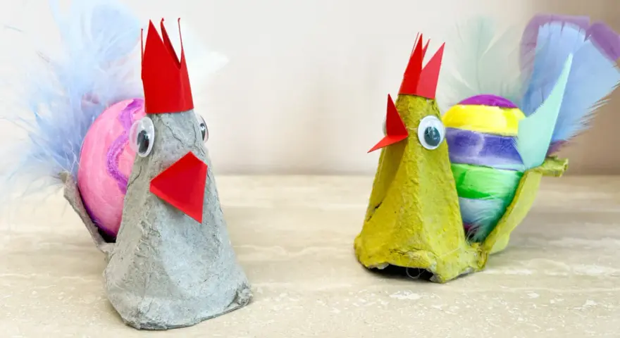 Två påskkycklingar gjorda av äggkartonger, med färgglada ägg och fjädrar. Ett roligt pyssel för påsk barn.