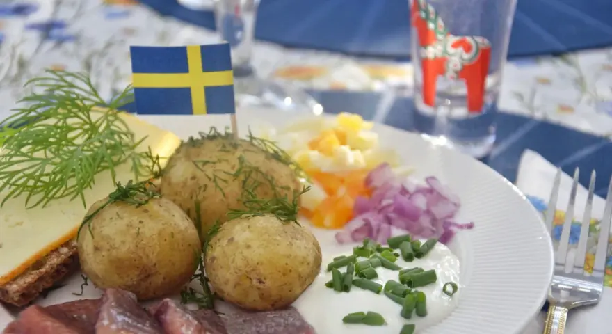 En tallrik med sill, färskpotatis, ost och dill. En svensk flagga vajar stolt. Perfekt mat midsommar!