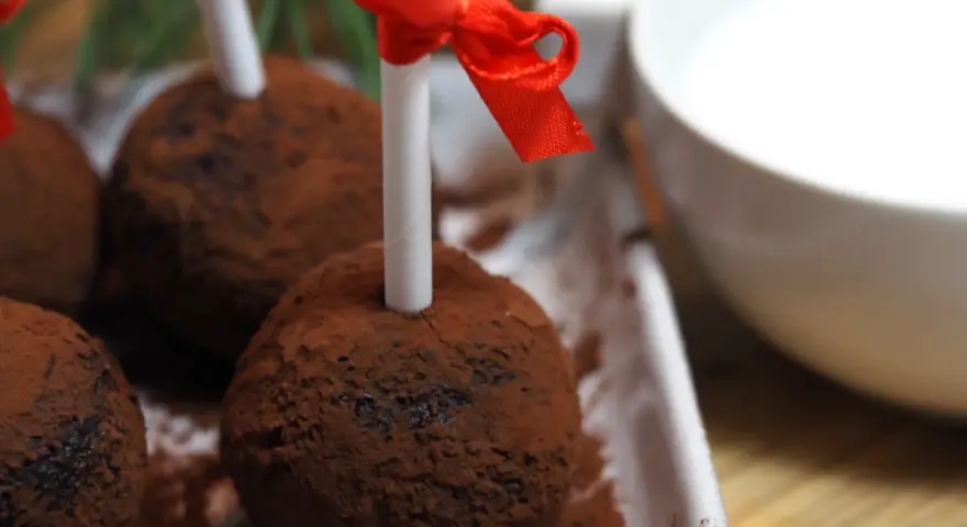 Chokladbollar på pinne, pudrade med kakao, redo att doppas i varm choklad. Röda band pryder pinnarna.