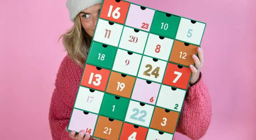 En person med en stickad tröja och mössa håller upp en färgglad julkalender. En perfekt julkalender diy att skapa själv!