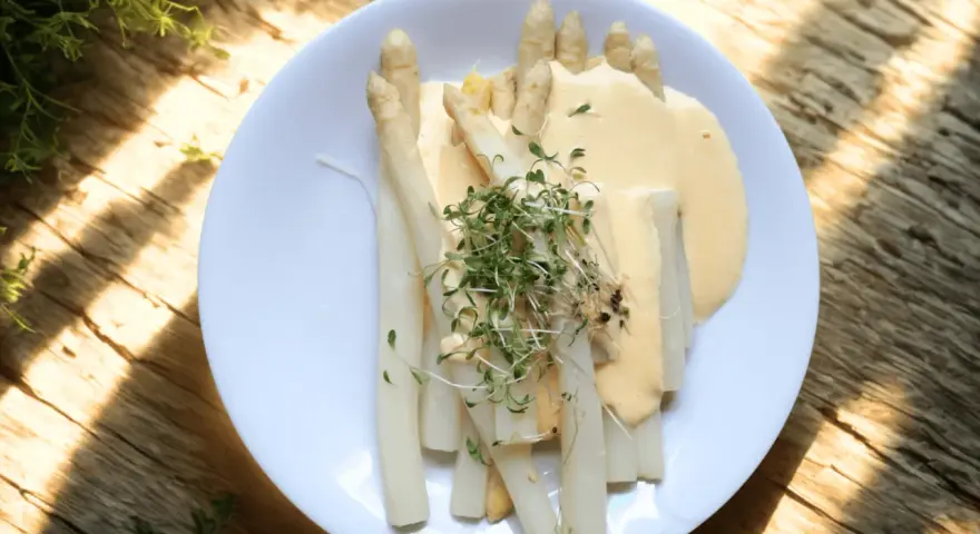 En tallrik med vit sparris, täckt av en krämig sås och toppad med färska groddar. En klassisk svensk vårrätt.