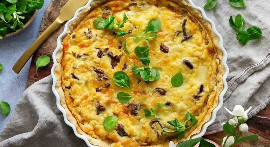 En gyllene kantarellpaj, perfekt för ett höstligt kantarellpaj recept. Garnerad med färska gröna blad och serverad med en gyllene kniv.