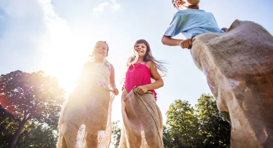 Barn hoppar säcklöpning i solsken, en klassisk midsommaraktivitet. En del av en femkamp midsommar.