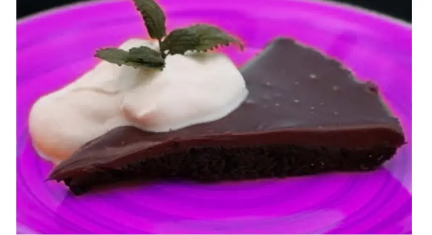 En bit kladdkaka med vispgrädde och mynta på en lila tallrik. Perfekt för en kladdkaka dag!