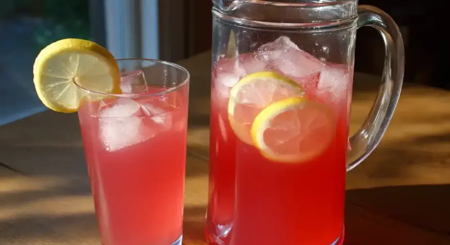En karaff och ett glas med rosa rabarbersaft, is och citronskivor. Perfekt för ett enkelt rabarbersaft recept.