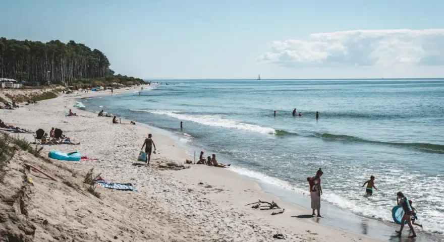 Människor njuter av solen och havet på sveriges finaste strand. En segelbåt syns i fjärran.