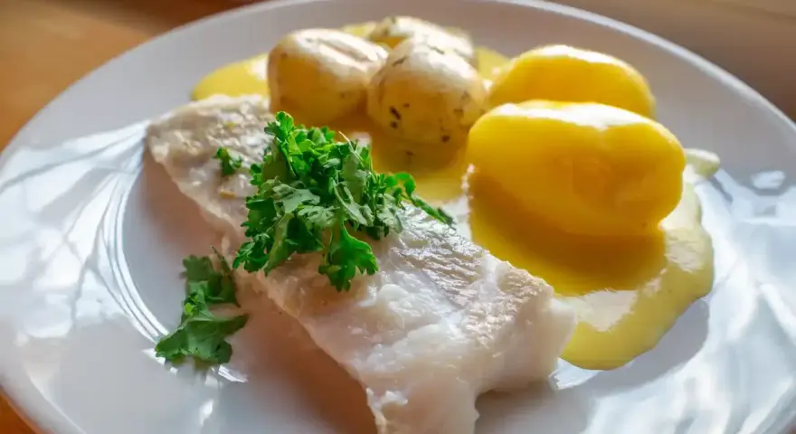 En portion rimmad torsk med kokt potatis och en krämig sås, garnerad med färsk persilja.